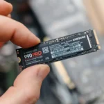 Man-holding-Samsung-990-PRO-SSD-between-fingers-over-exposed-laptop-hero
